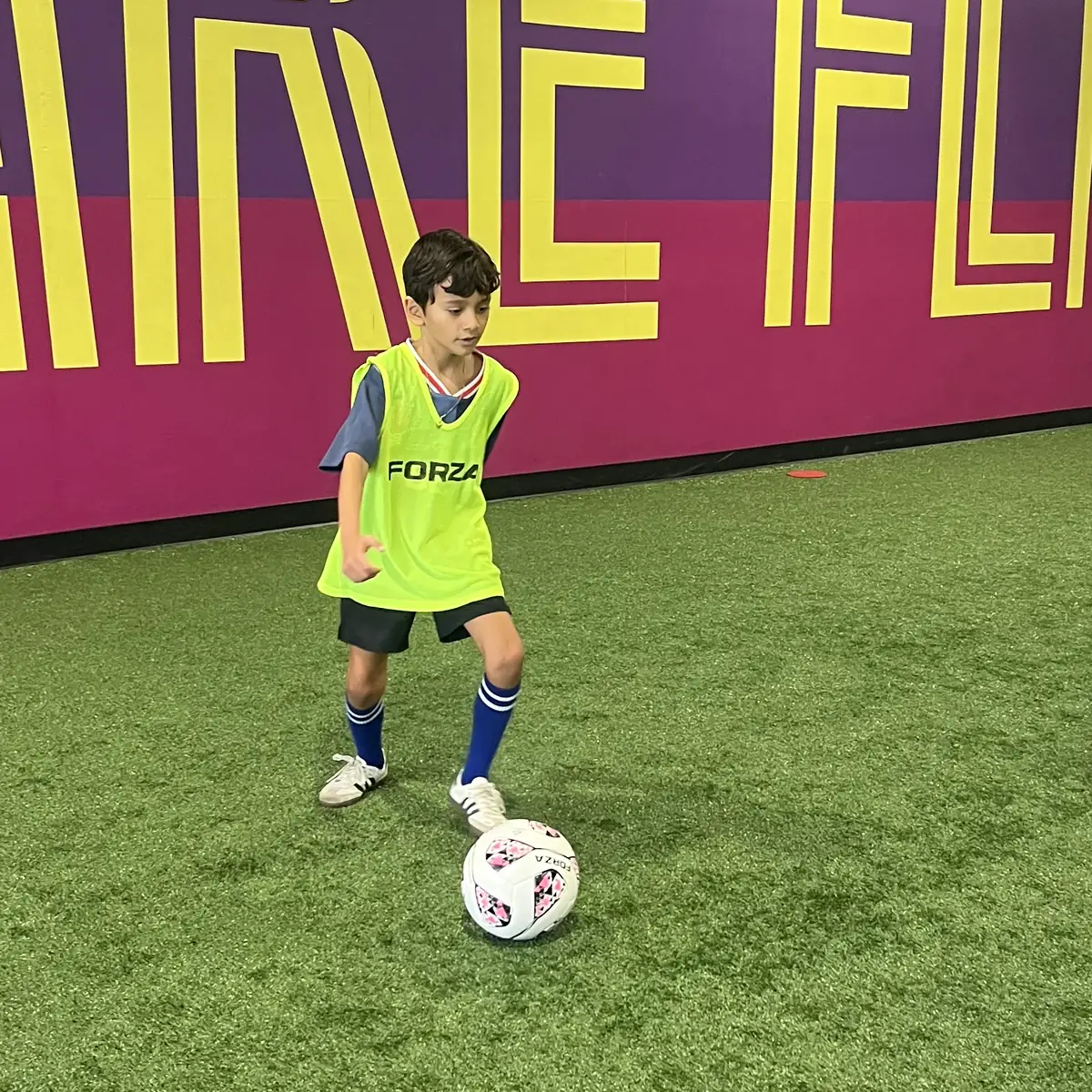 A young player dribbling a soccer ball on Soccer HQ's indoor turf during class