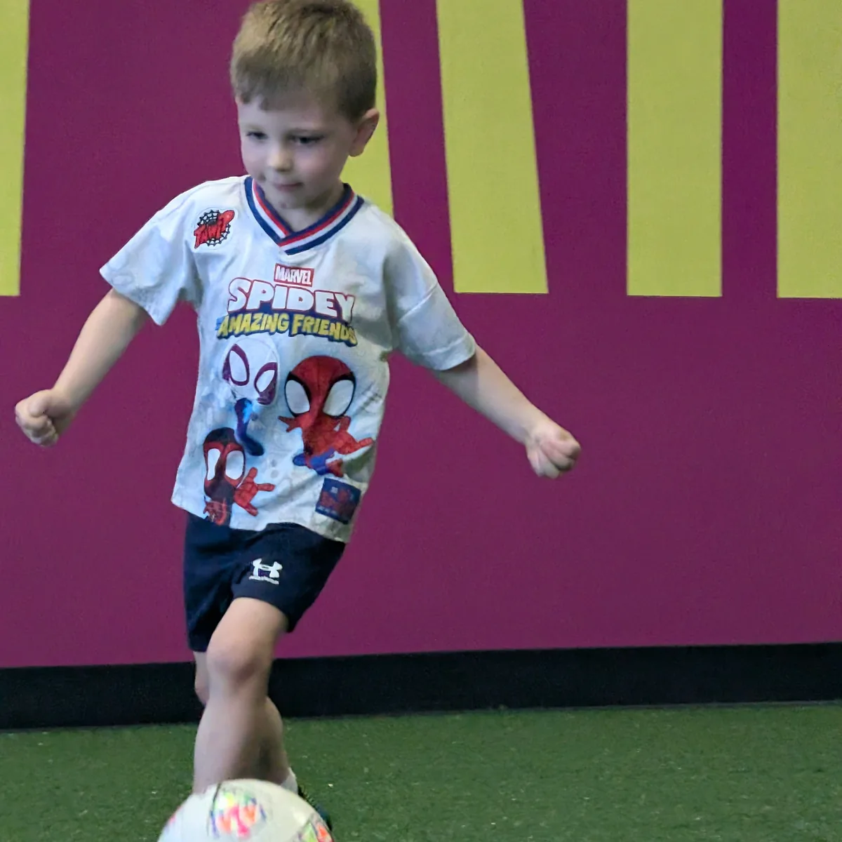 A young child dribbling a soccer ball on Soccer HQ's indoor turf during a Little Kicks class